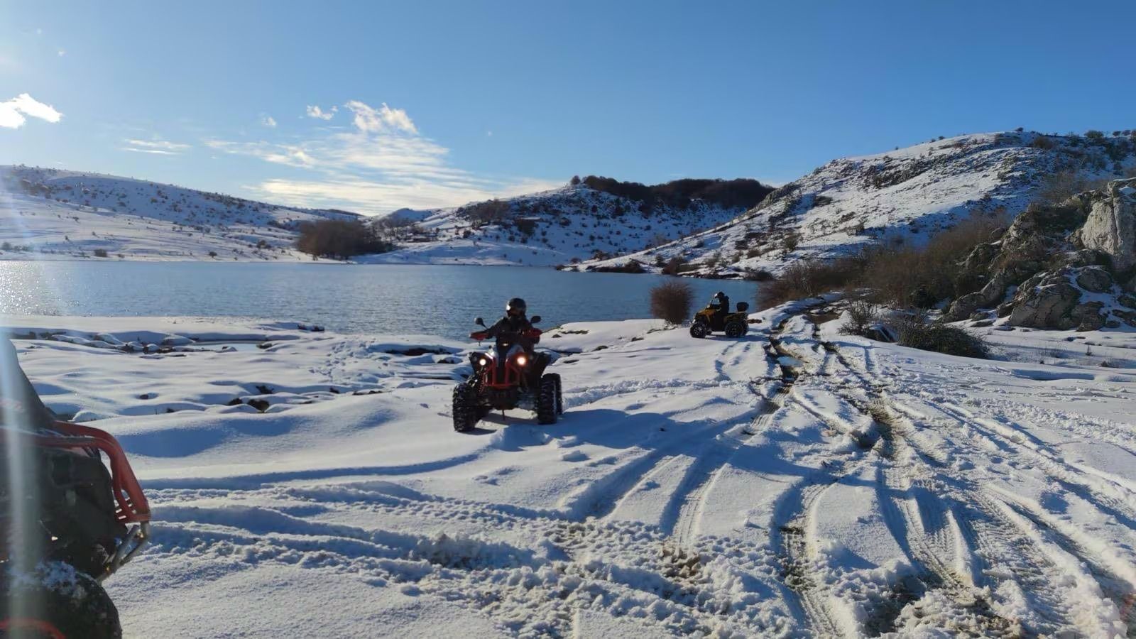 Quad che percorrono un paesaggio innevato vicino a un lago, sotto un cielo azzurro.