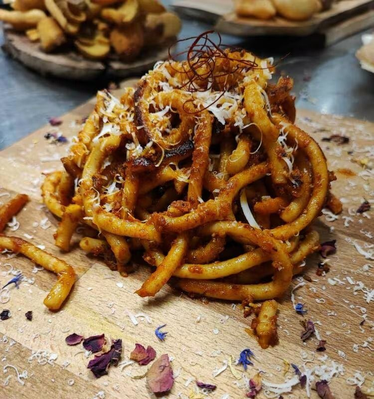 Piatto di pasta, su un tagliere di legno. Tagliatelle spesse in salsa rossa, condite con formaggio grattugiato e peperoncino in fiocchi.