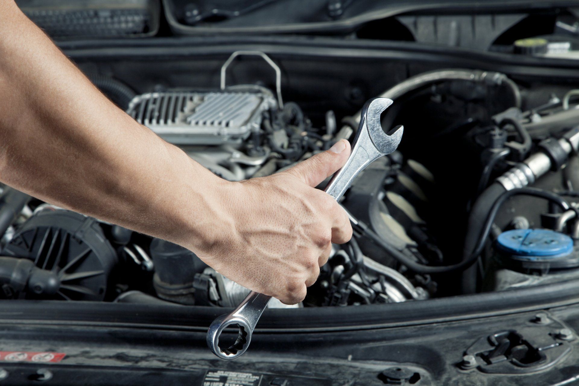 Mechanic's hand holding a wrench, working on a car engine.