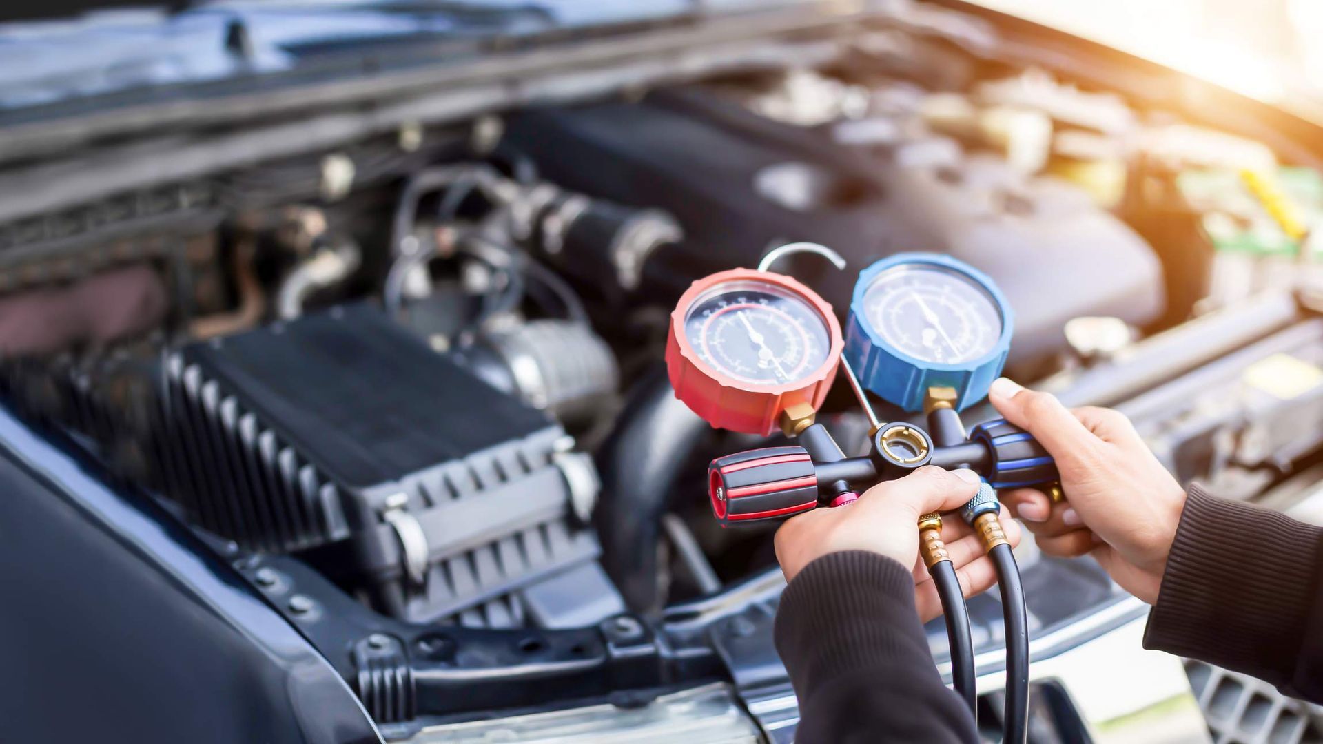 Person using a manifold gauge set to check a car's air conditioning system under the hood.