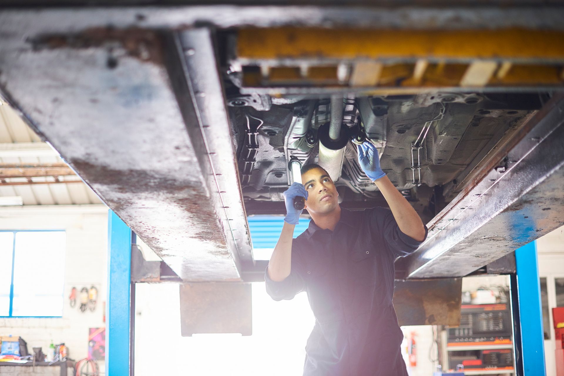 Auto mechanic inspecting undercarriage of lifted car in professional vehicle repair workshop.