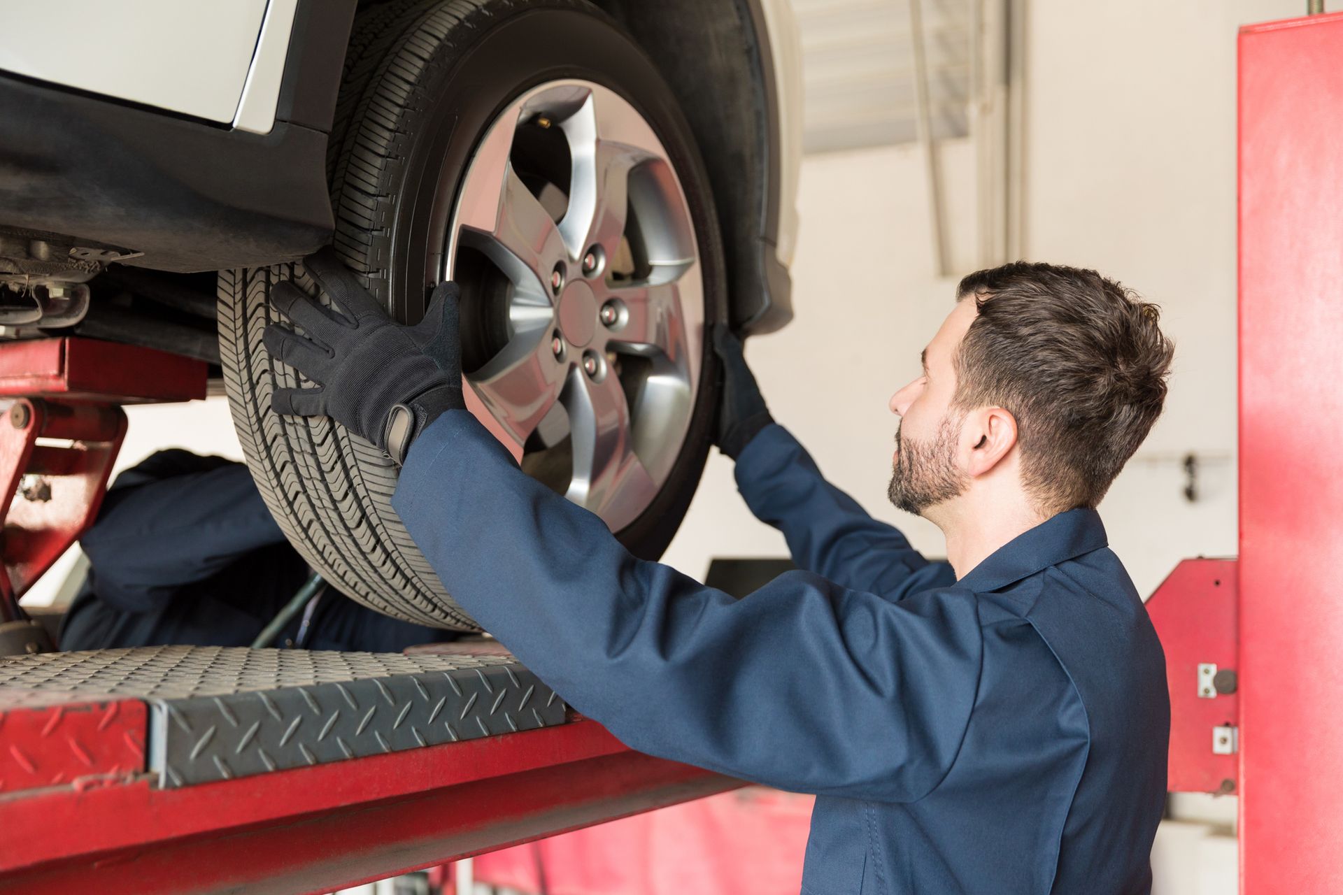 Person installing car tire on vehicle lift during professional wheel service at auto repair shop bay.
