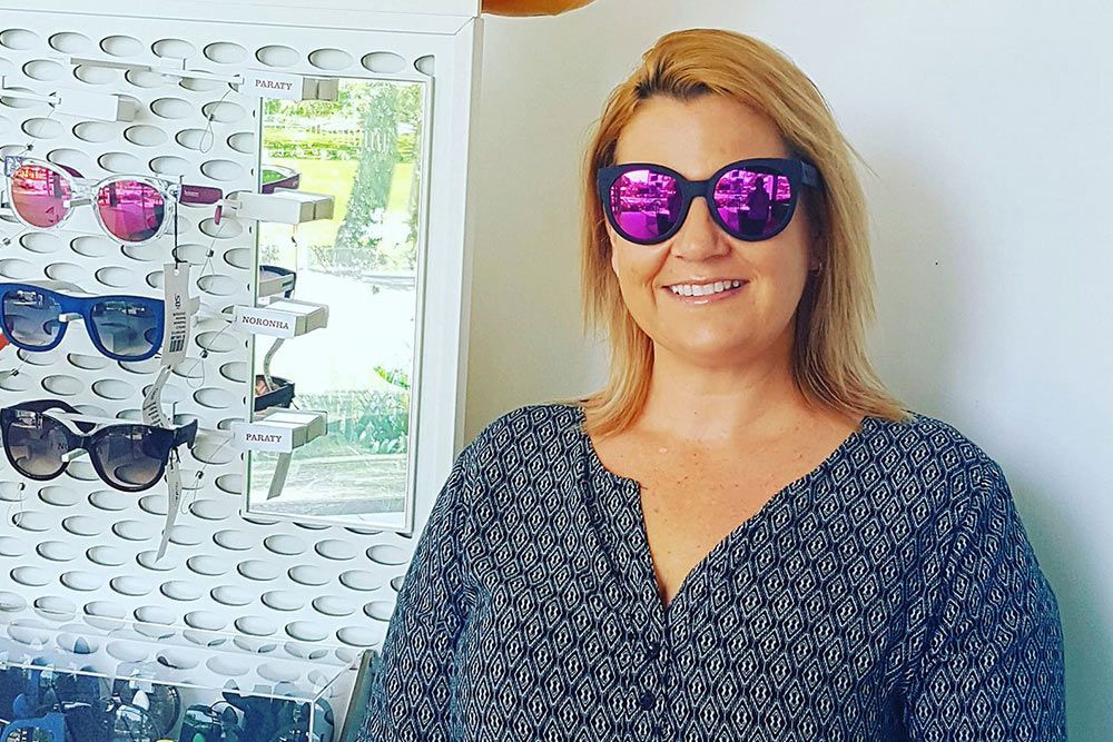 A Woman Wearing Sunglasses Is Standing In Front Of A Wall Of Sunglasses — Central Coast Eyecare In Gosford, NSW