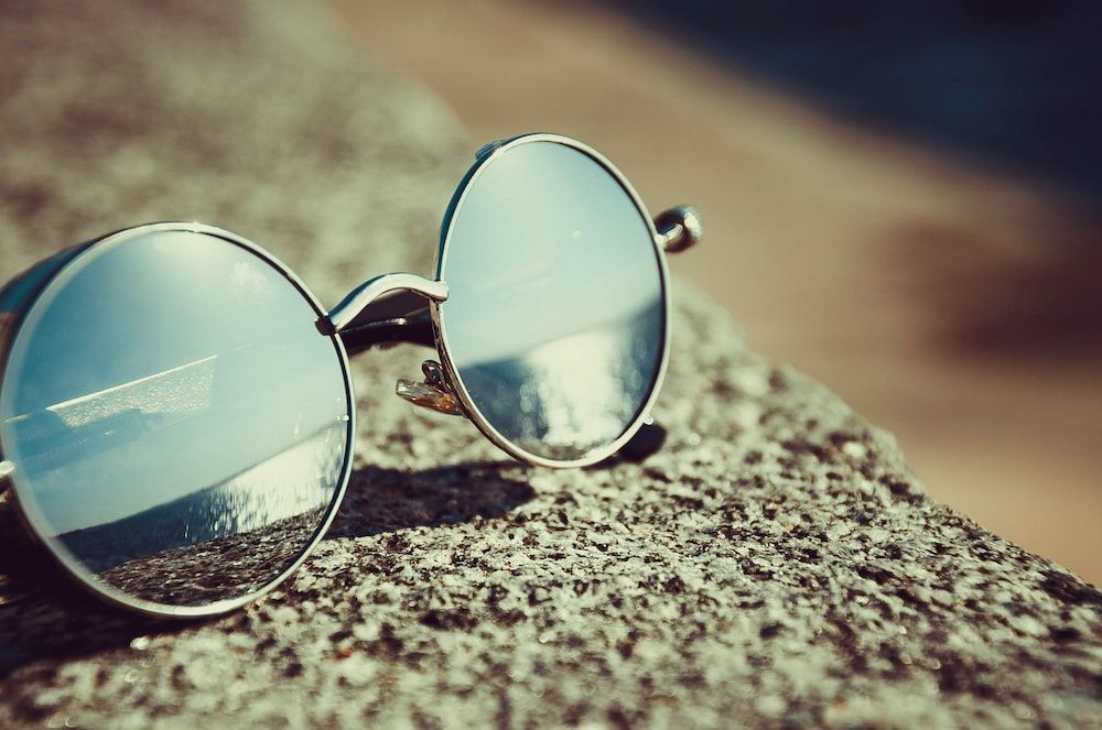 A Pair Of Round Sunglasses Sitting On Top Of A Rock — Central Coast Eyecare In Gosford, NSW