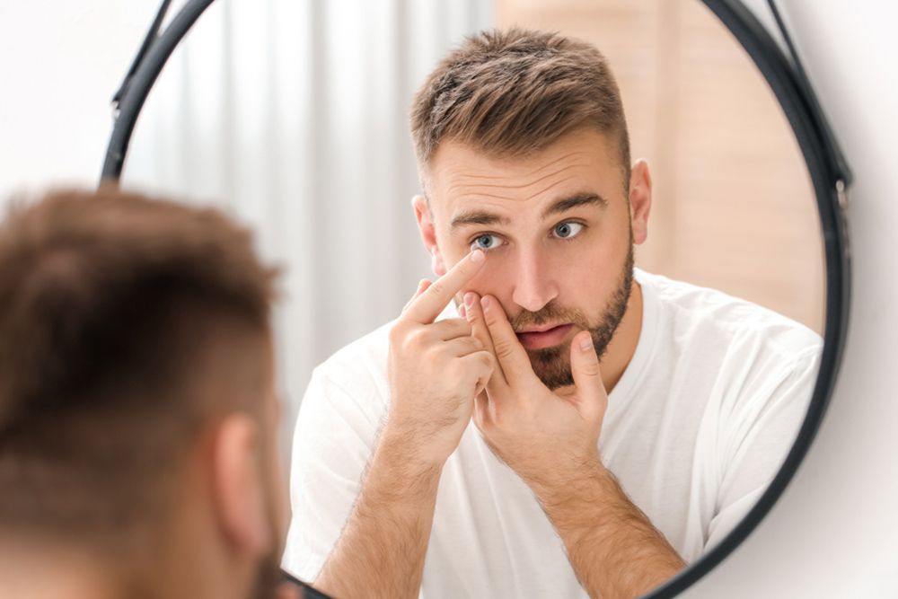 A Man Is Putting Contact Lenses On His Eyes In Front Of A Mirror — Central Coast Eyecare In Gosford, NSW