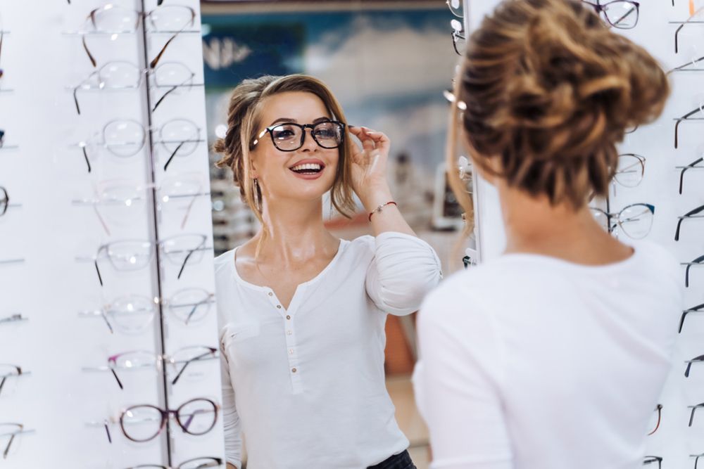 Woman Smiling In The Mirror While Trying Glasses — Central Coast Eyecare In Gosford, NSW