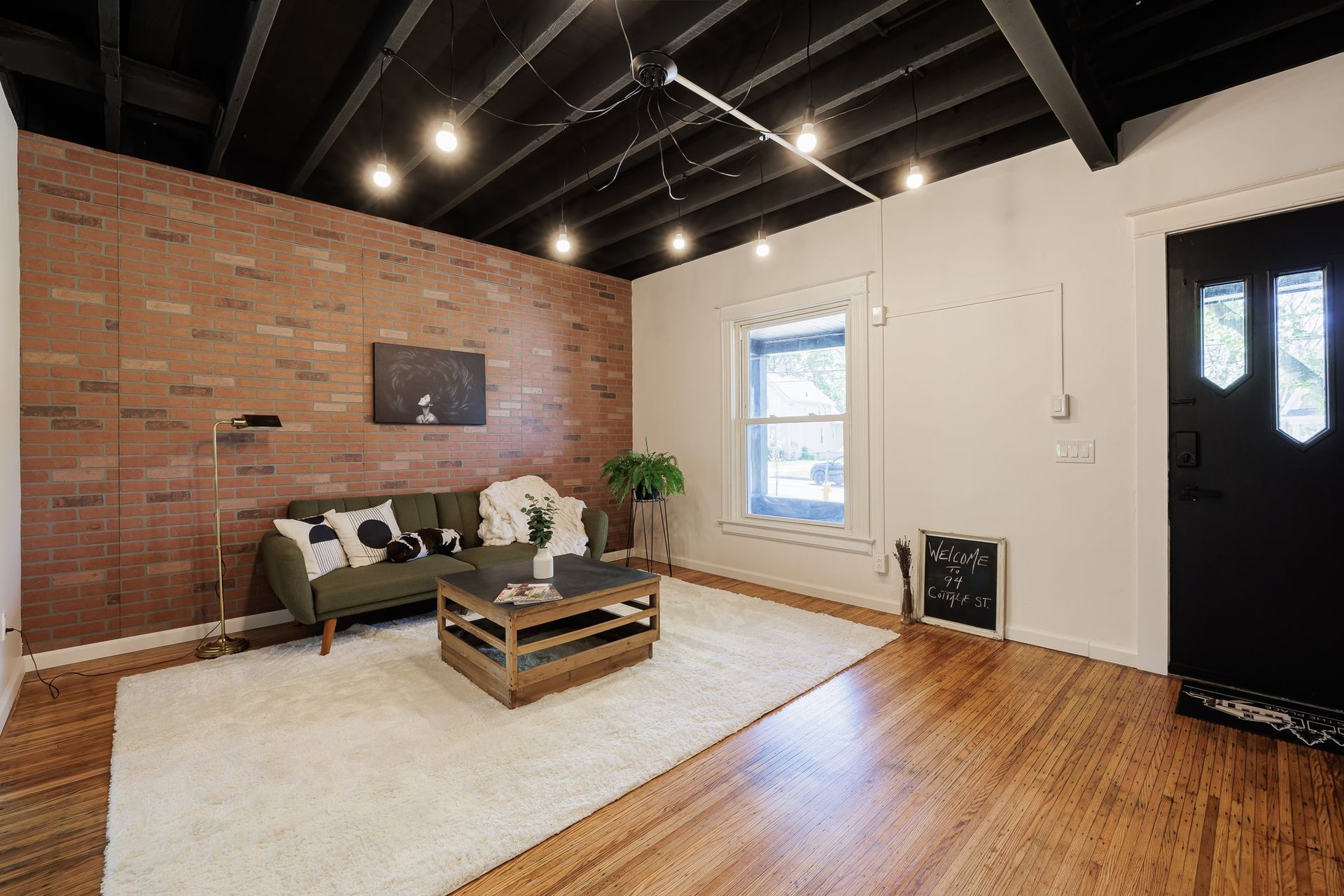 A living room with a couch , coffee table , rug and brick wall.