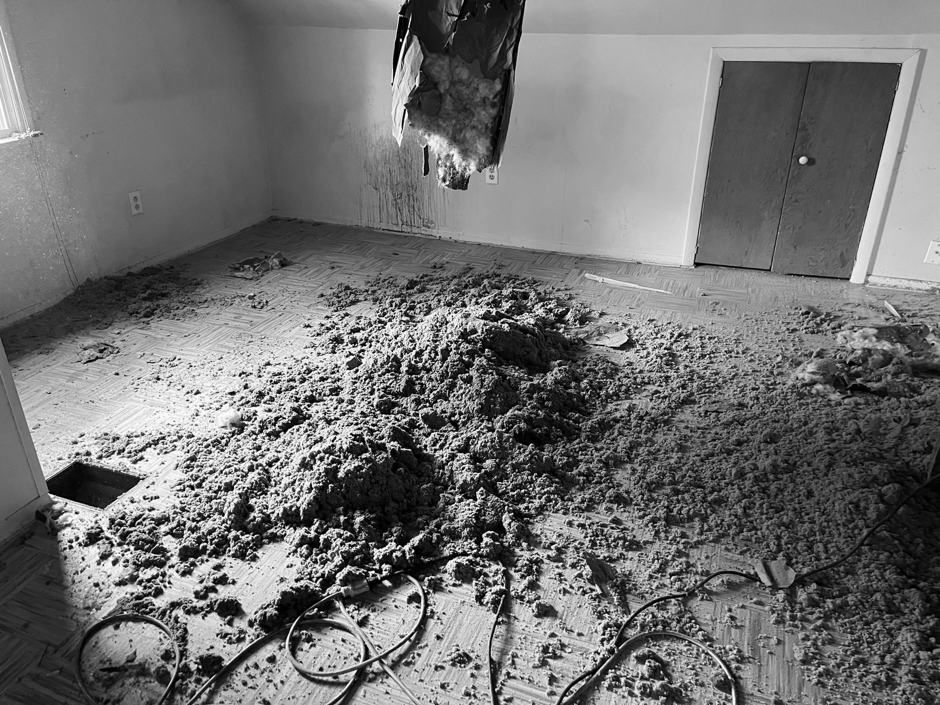 A room with debris scattered on the floor from a large hole in the ceiling, revealing insulation and structural damage.
