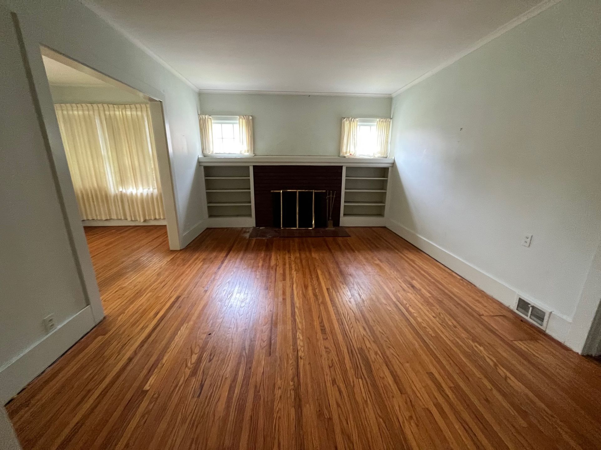 An empty living room with hardwood floors and a fireplace.