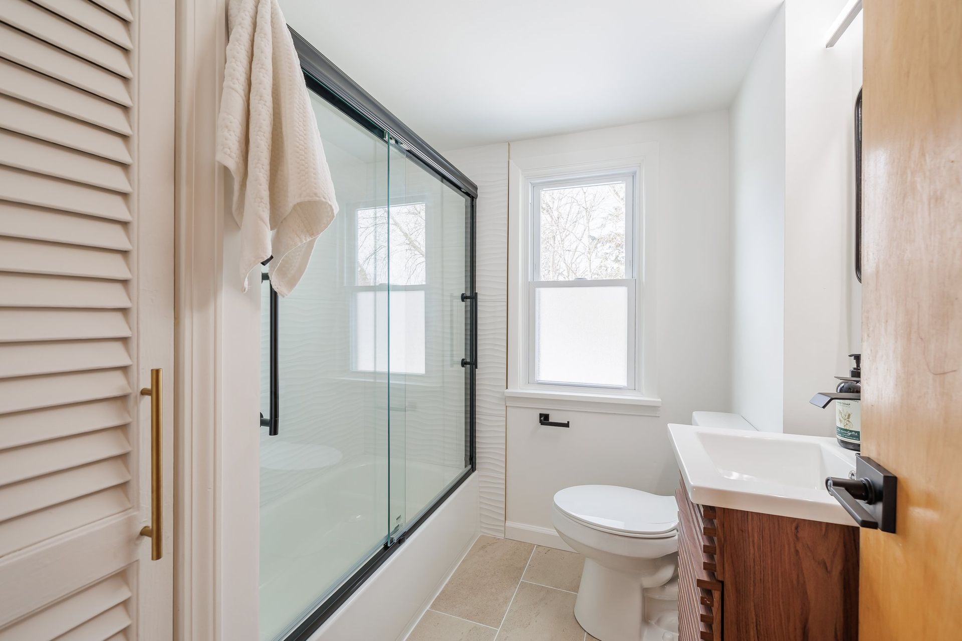 A bathroom with a toilet , sink , shower and window.