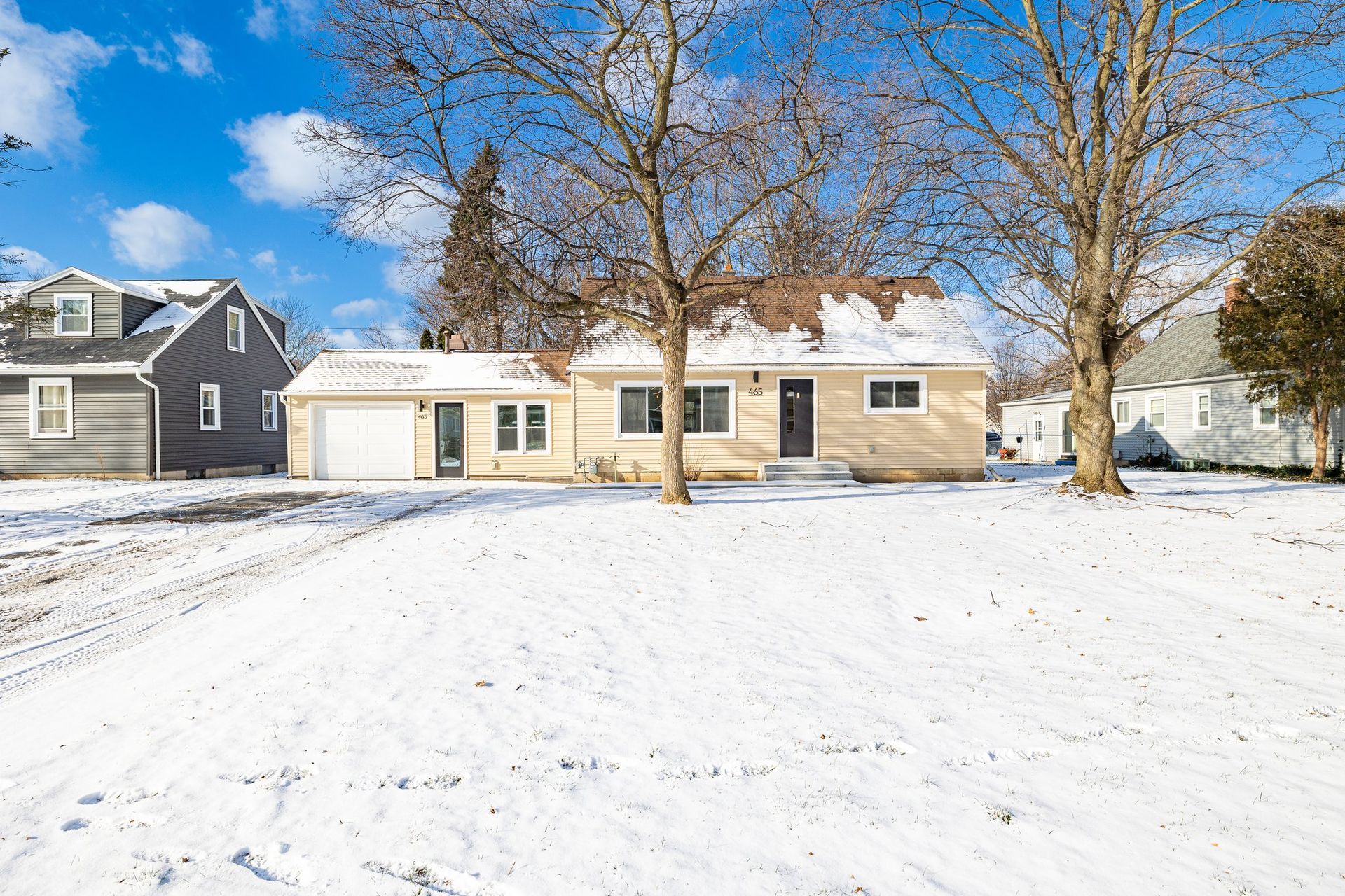 A house with a garage is surrounded by snow and trees.