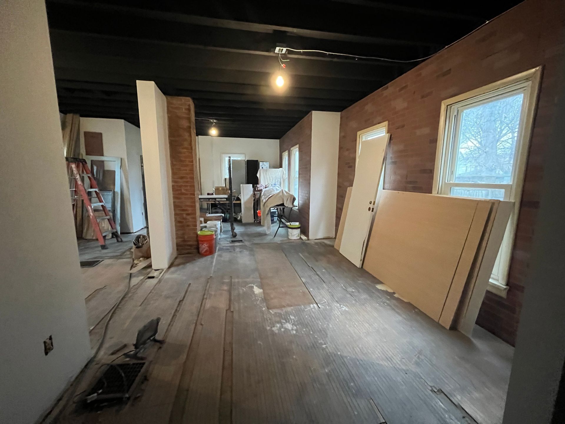 A large room with a wooden floor and brick walls is being remodeled.