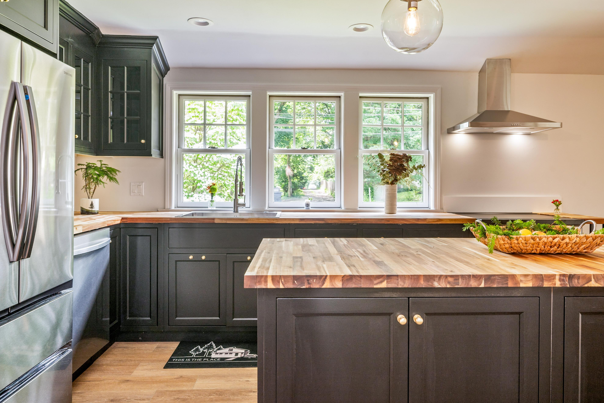 A kitchen with black cabinets , a stainless steel refrigerator , a wooden counter top , and a large island.