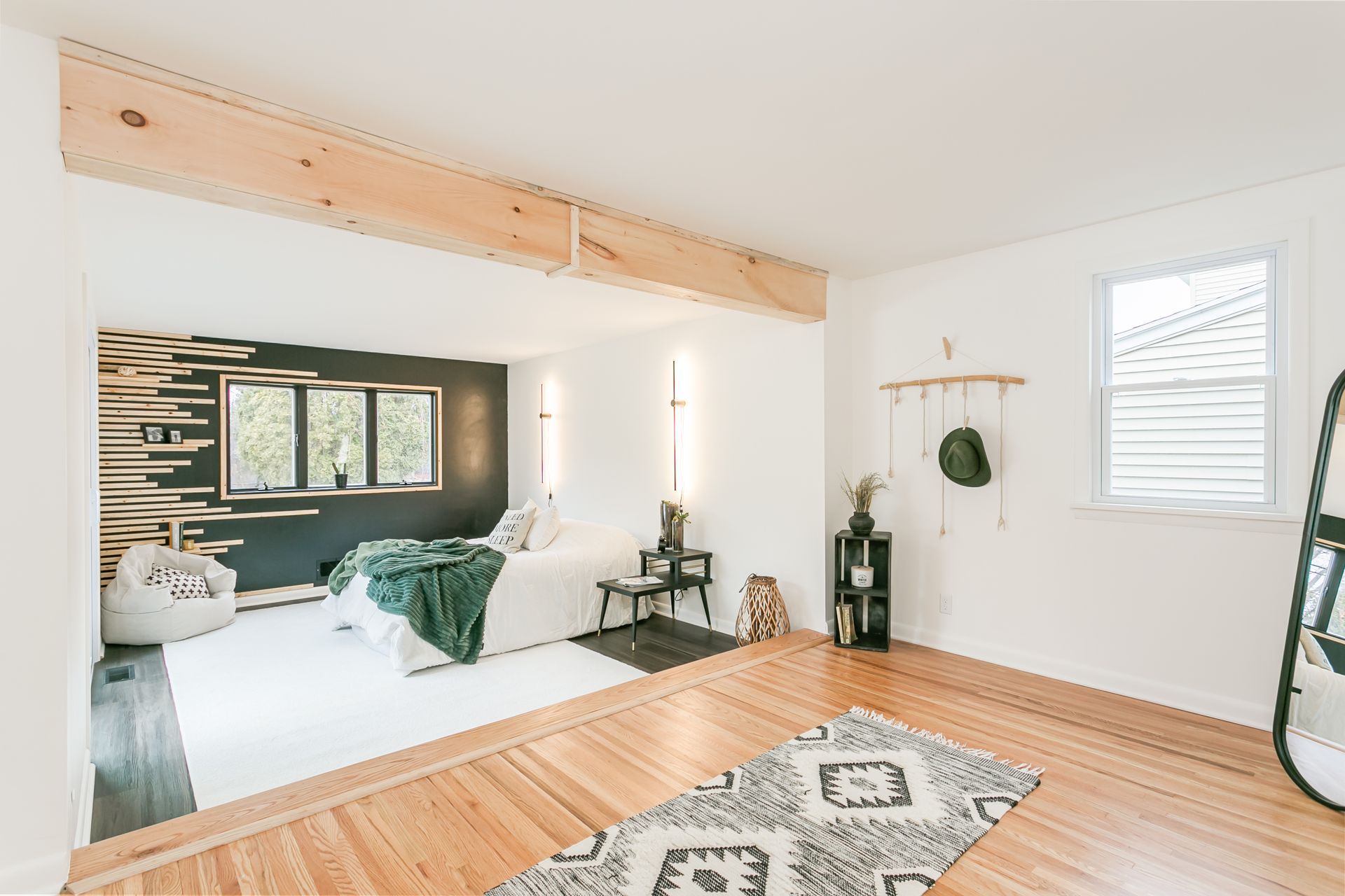 A bedroom with hardwood floors , a bed , a rug and a mirror.