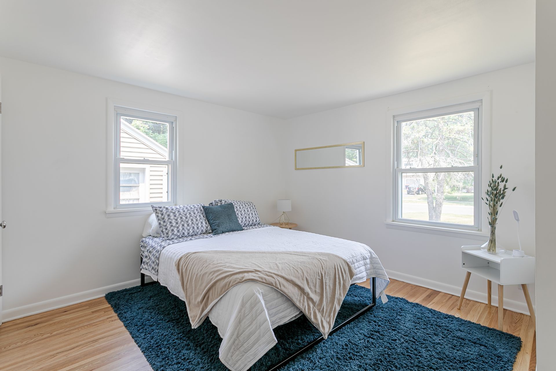 A bedroom with a bed , rug , window and mirror.