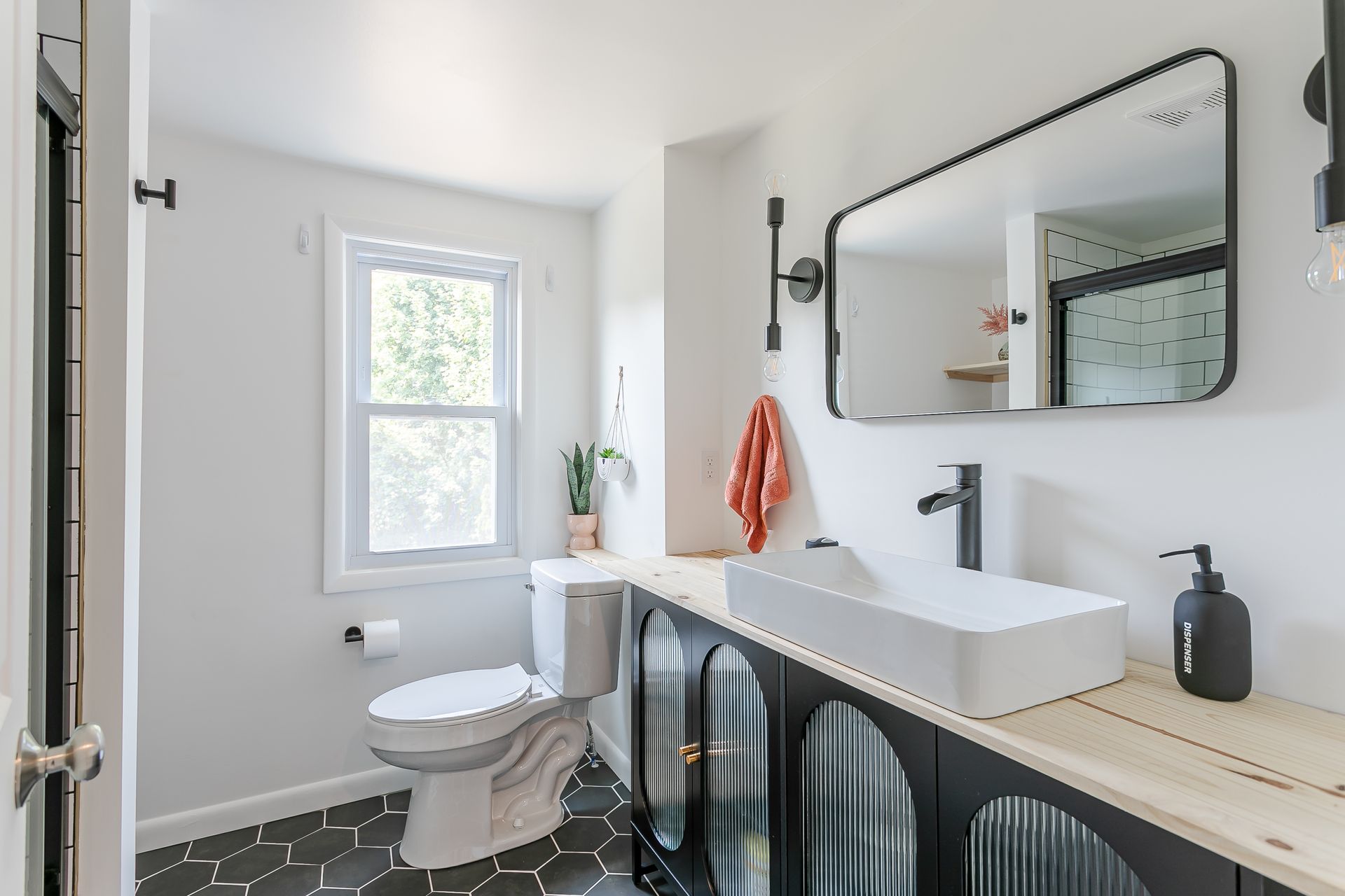 A bathroom with a toilet , sink , mirror and window.