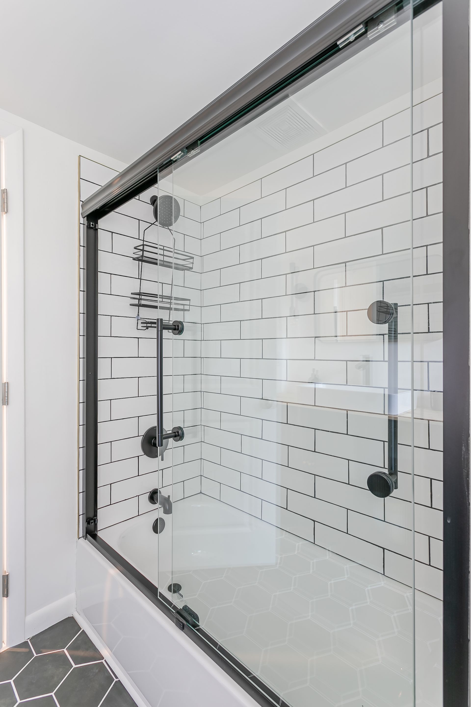 A bathroom with white tiles and a sliding glass shower door.