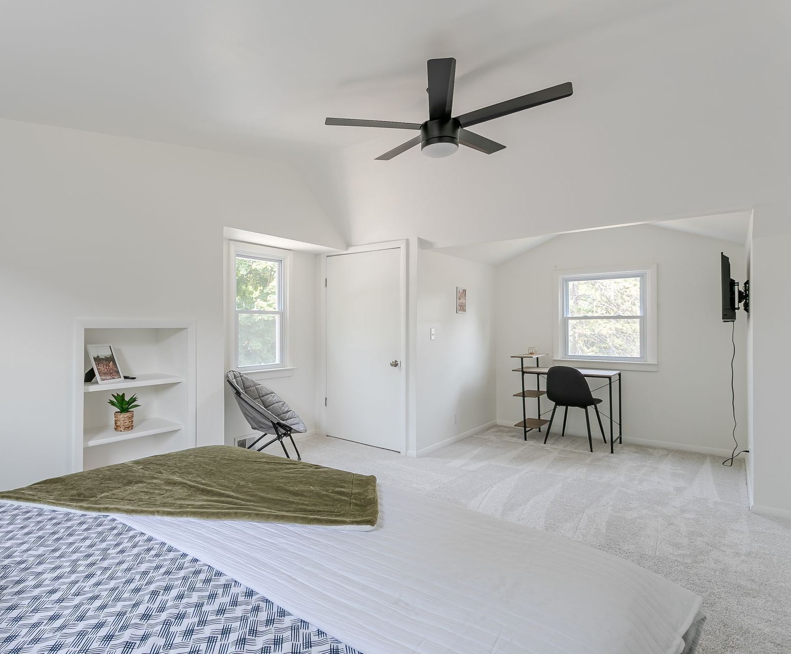 A bedroom with a bed , desk , chair and ceiling fan.