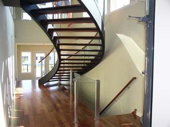 A curved staircase with a glass railing in a hallway