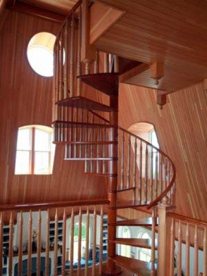 A wooden spiral staircase in a house with a round window
