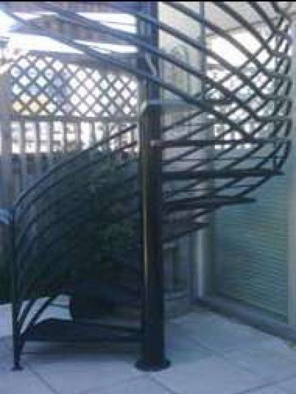 A spiral staircase is sitting on a patio next to a window.