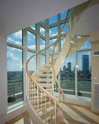 A spiral staircase in a room with lots of windows and a view of the city.