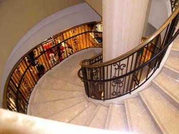 A spiral staircase with a wrought iron railing and marble steps