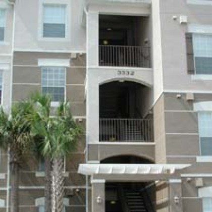 A large apartment building with stairs and balconies and palm trees in front of it.