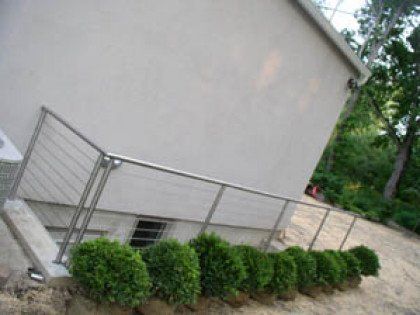 A white building with a stainless steel railing and bushes in front of it.