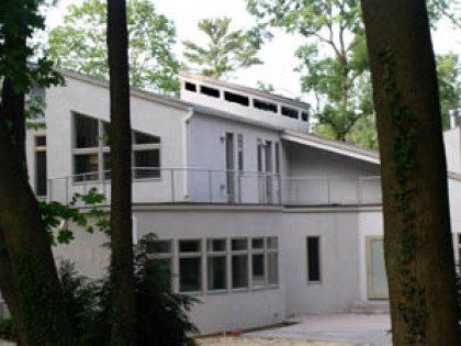 A white house with a balcony is surrounded by trees