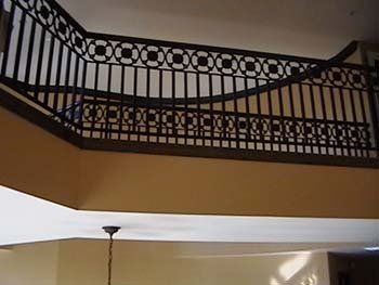 A staircase with a wrought iron railing and a chandelier hanging from the ceiling.