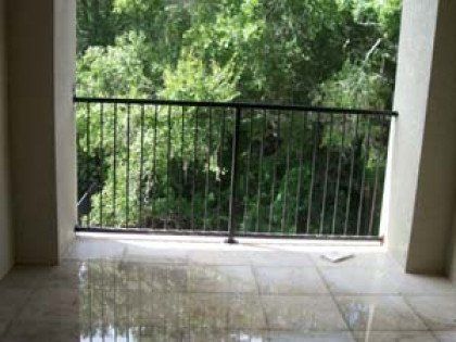 A balcony with a metal railing and trees in the background.