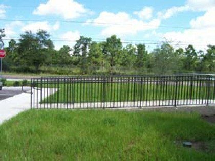 A metal fence surrounds a lush green field with trees in the background.