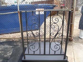 A wrought iron railing is sitting in front of a chain link fence.