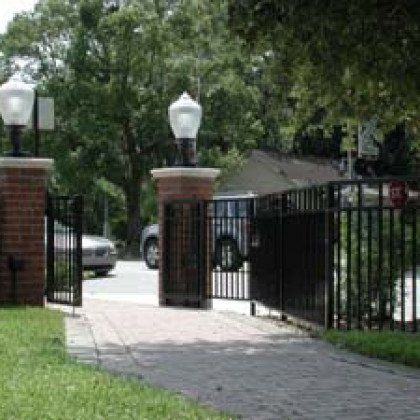 A brick walkway leading to a gate with lights on top of it.
