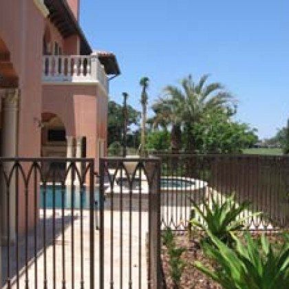 A house with a pool and palm trees behind a fence.