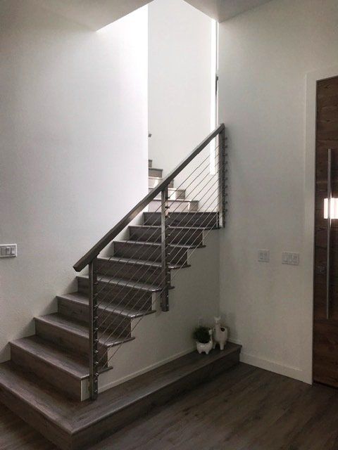A staircase with a stainless steel railing is in a hallway.