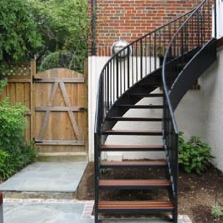 A black spiral staircase with wooden steps is next to a wooden gate.