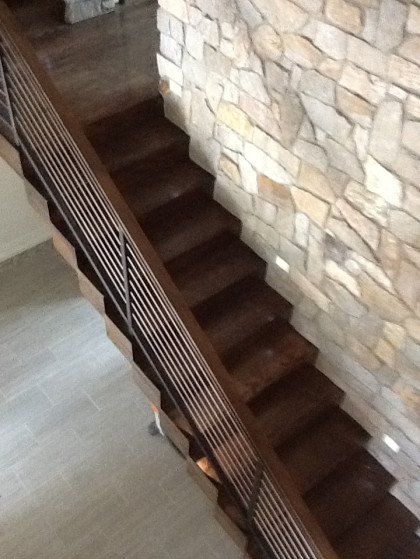 A wooden staircase with a metal railing in front of a stone wall.