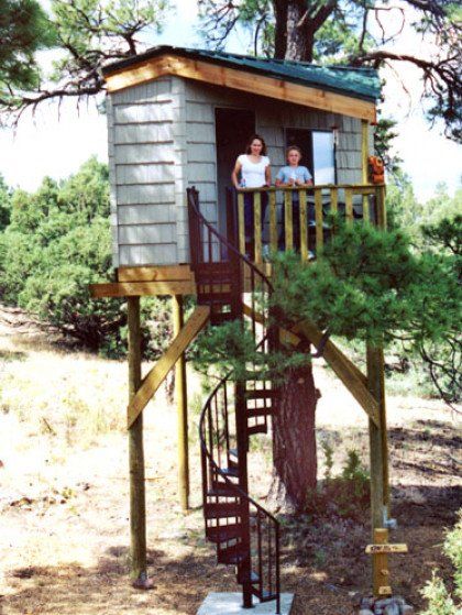 Two people standing on a tree house with a spiral staircase