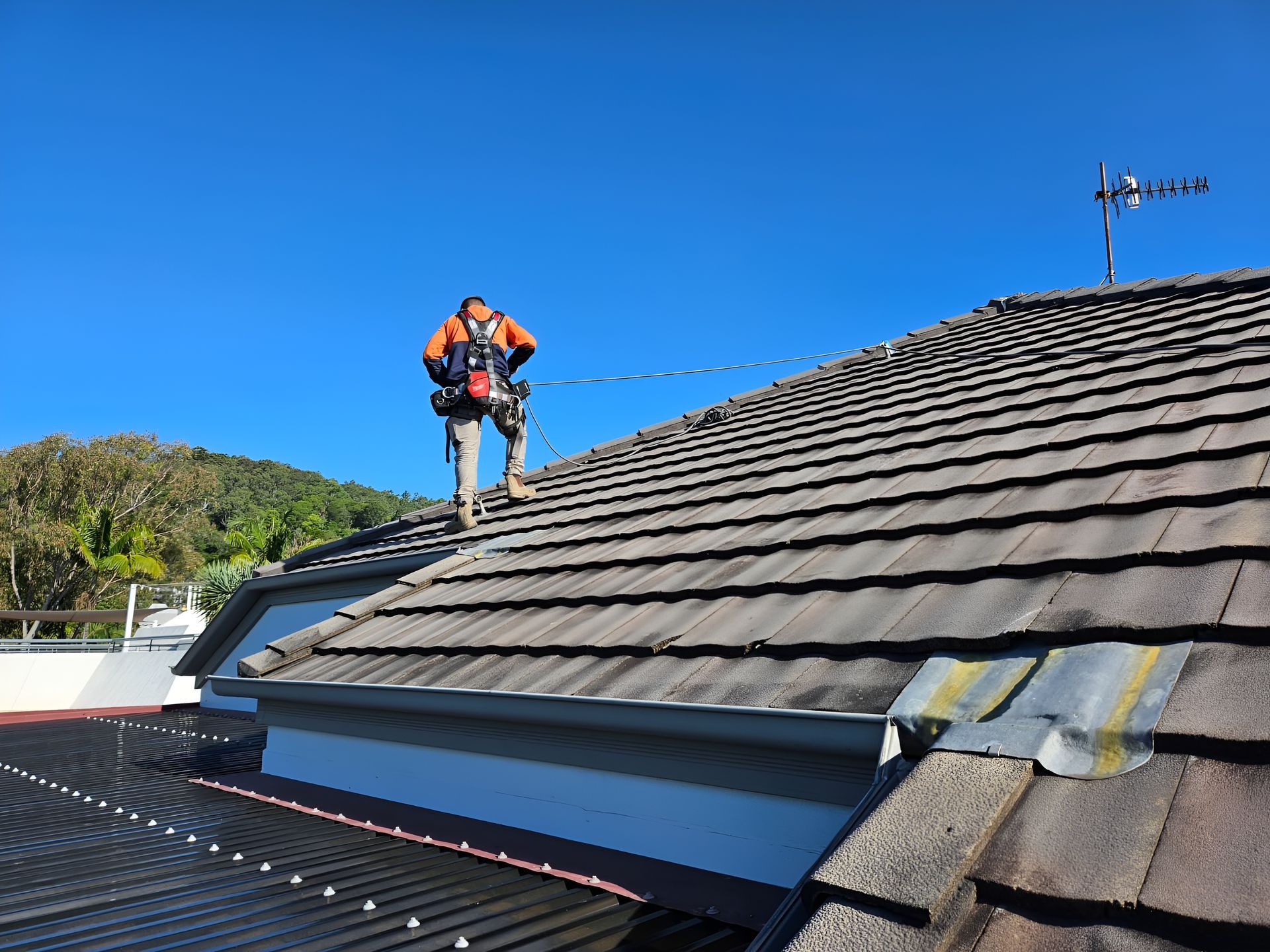 Roofer in Safety Harness on a Tile Roof, Blue Sky Backdrop — Australian Asset Compliance in Gympie, QLD