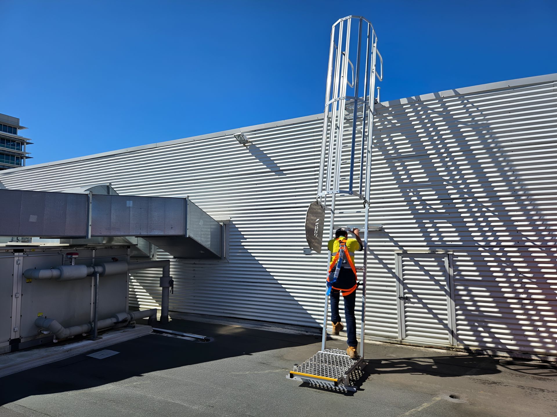 Person Wearing Safety Gear Climbing a Tall Ladder on a Rooftop, Sunny Day — Australian Asset Compliance in Gympie, QLD