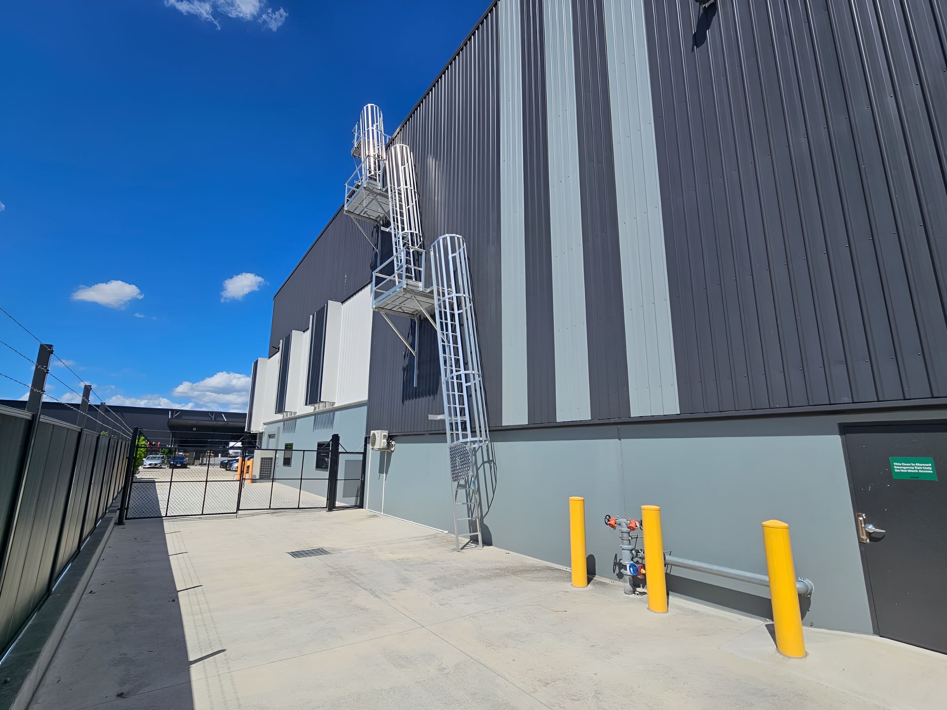 Exterior of industrial building with metal ladder/staircase attached. Gray and black panels, blue sky. — Australian Asset Compliance in Mackay, QLD