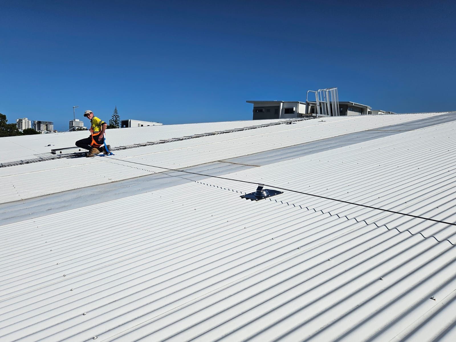 Worker on a white corrugated metal roof, wearing safety gear, with blue sky background. — Australian Asset Compliance in Glanmire, QLD