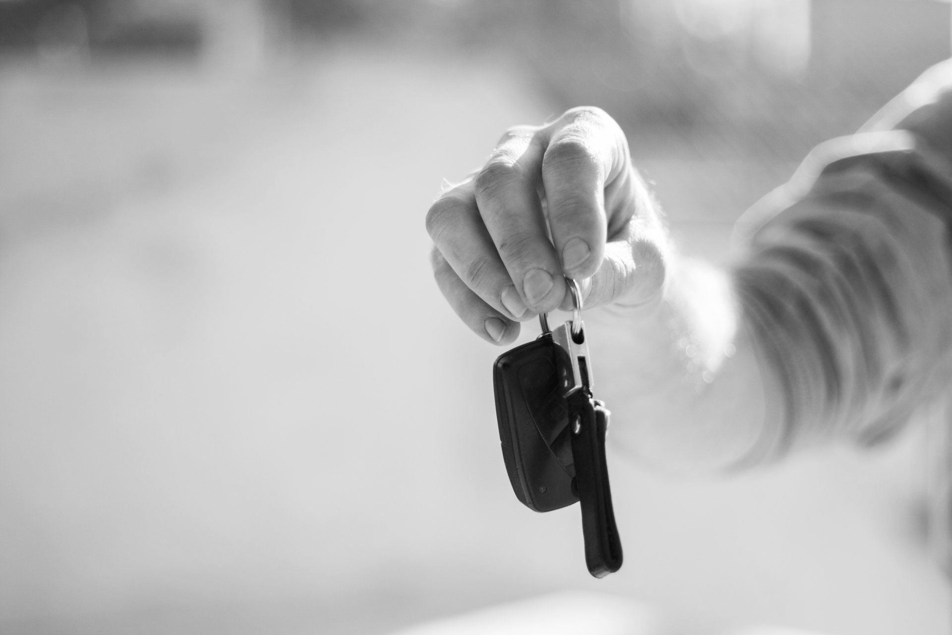 A person is holding a car key in their hand in a black and white photo.