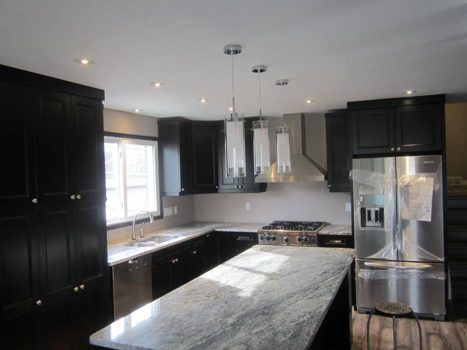 Modern kitchen with black cabinets, granite countertops, stainless steel appliances, and pendant lighting.