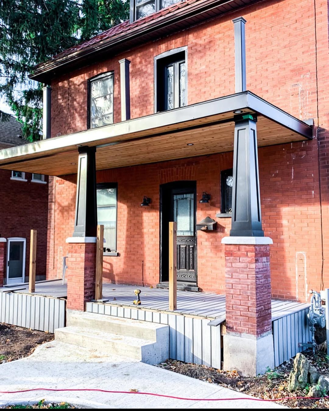 Red brick house with a porch and steps. Black and wooden accents, sunny outdoor setting.