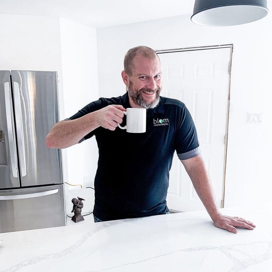 Man in black shirt holding coffee mug, smiling in a kitchen.