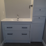 White bathroom vanity with drawers, sink, and cabinet. Black hardware. Gray walls.