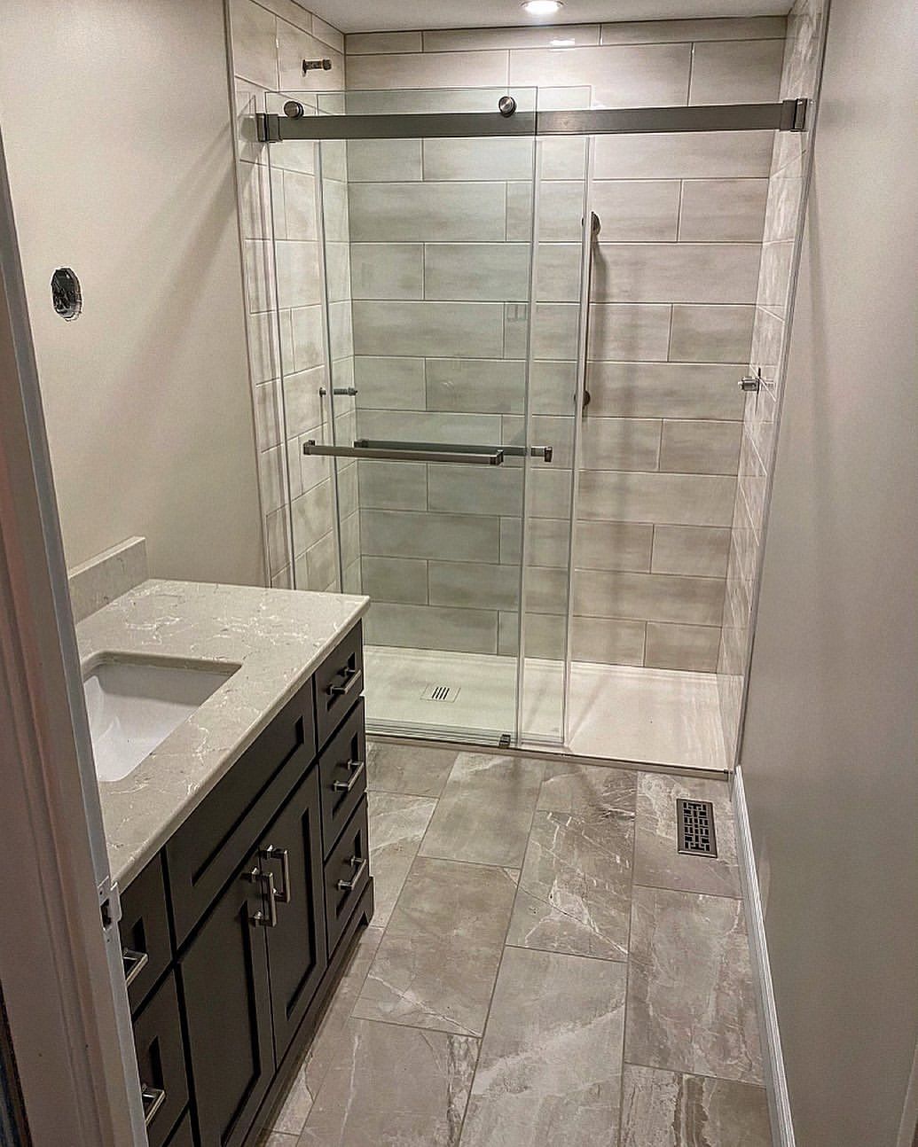 Bathroom with gray vanity, tiled floor and shower with glass doors.
